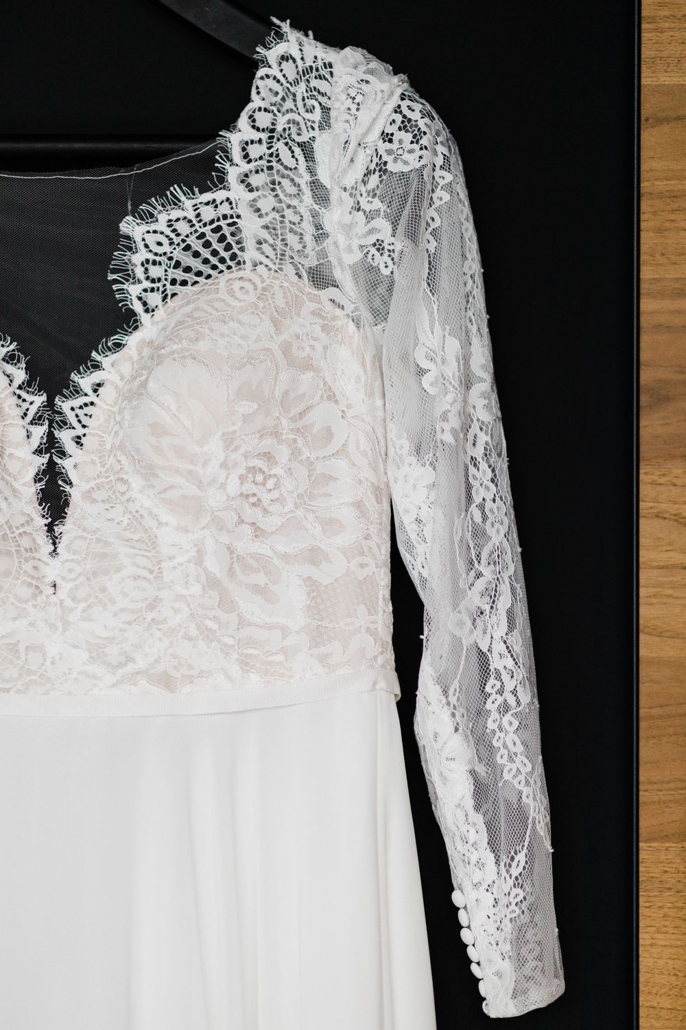 Delicate white lace wedding dress with long sleeves displayed against dark background.