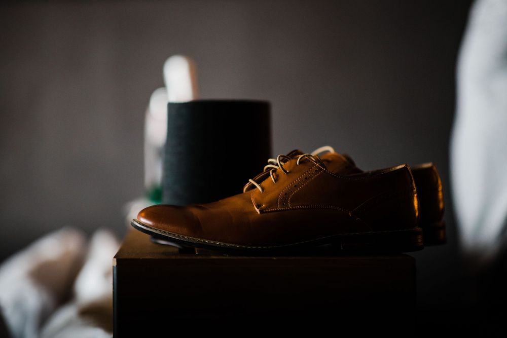A brown leather dress shoe sits atop a dark box in moody lighting.