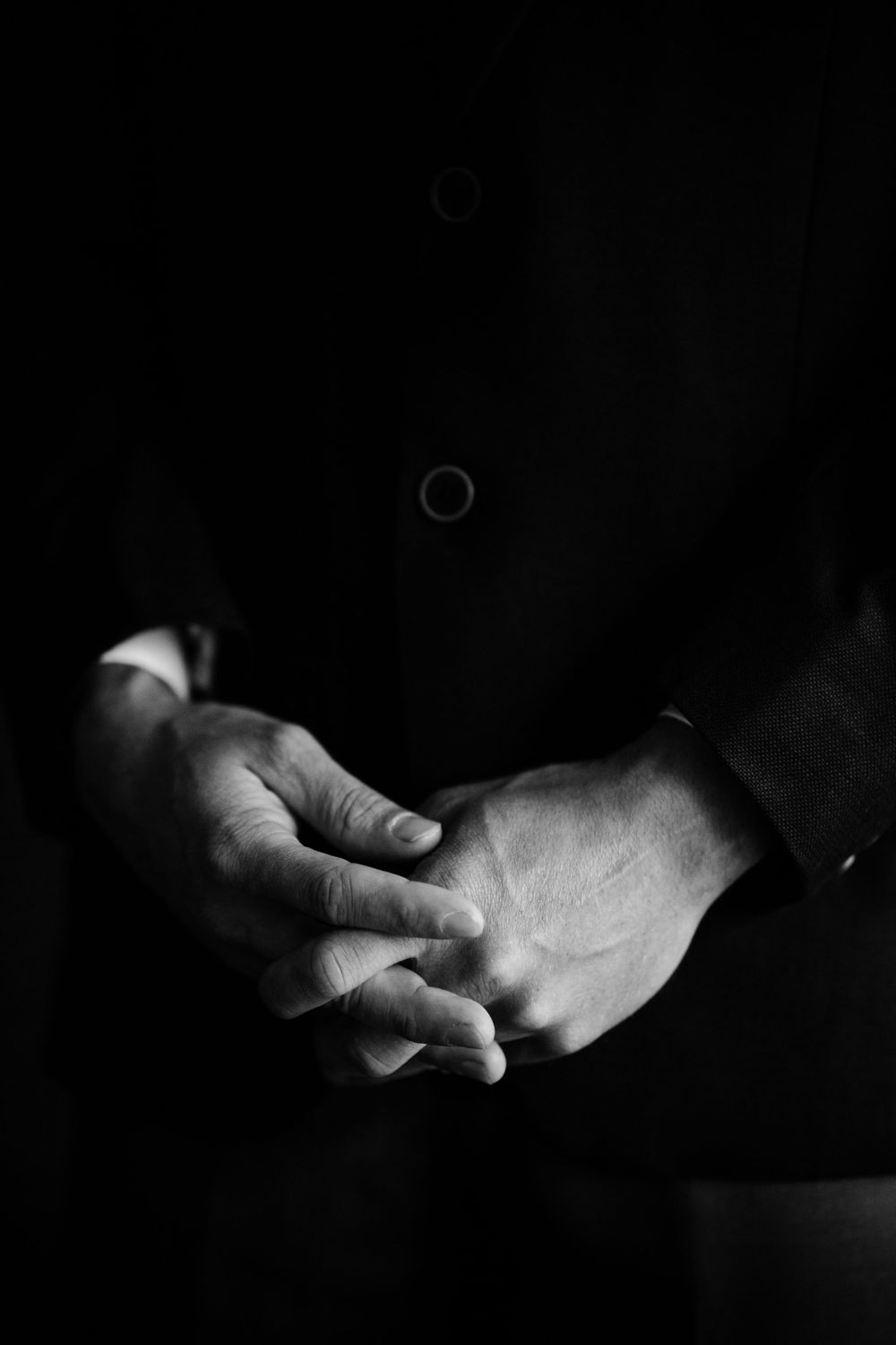 Black and white close-up of clasped hands in formal attire.