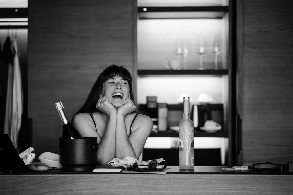 Person laughing joyfully at bar counter with drinks and candles in background.