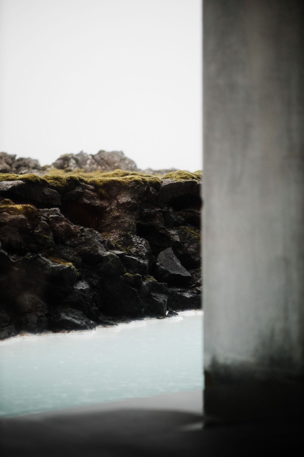 Rocky cliff face and misty water viewed through concrete structures.
