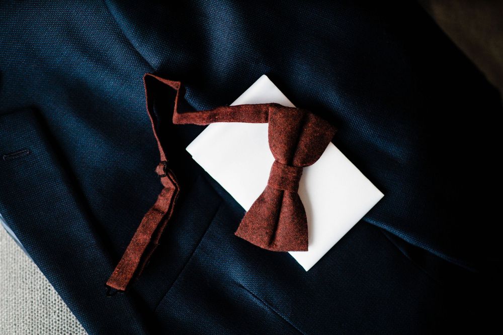 A burgundy bow tie rests on white paper against dark fabric.