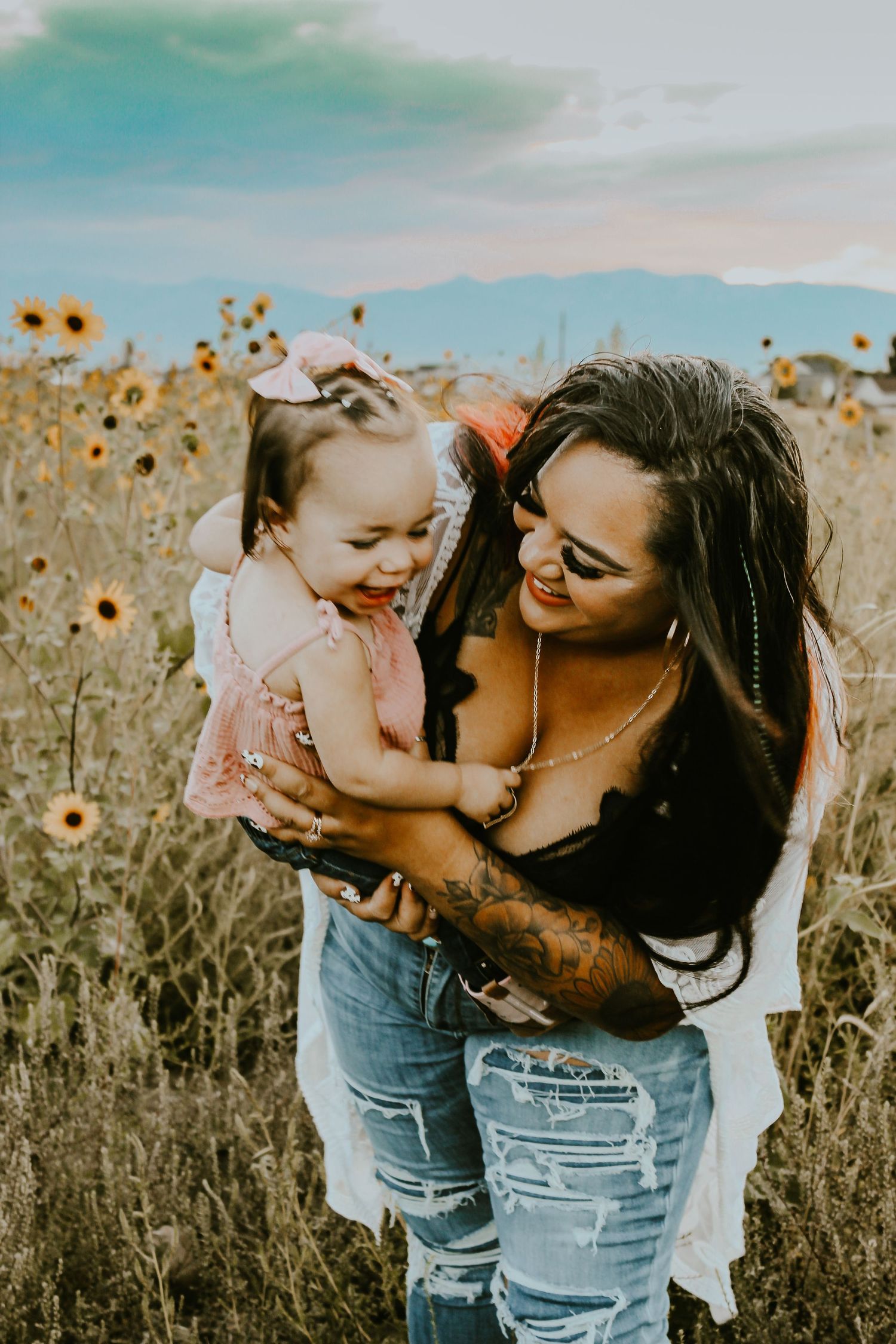 A mother holds her laughing toddler in a sunflower field at golden hour.