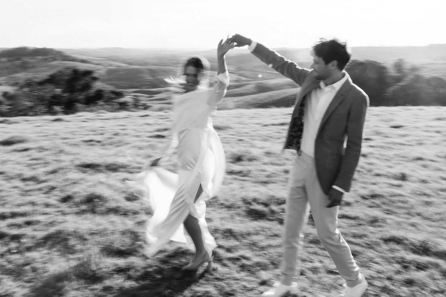 Couple dancing playfully in field during wedding photoshoot.