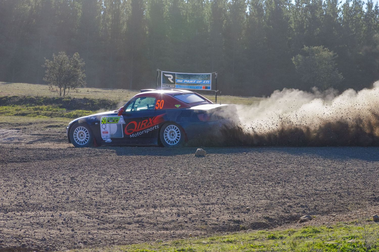 Race car creating dust trail while drifting through dirt track corner.