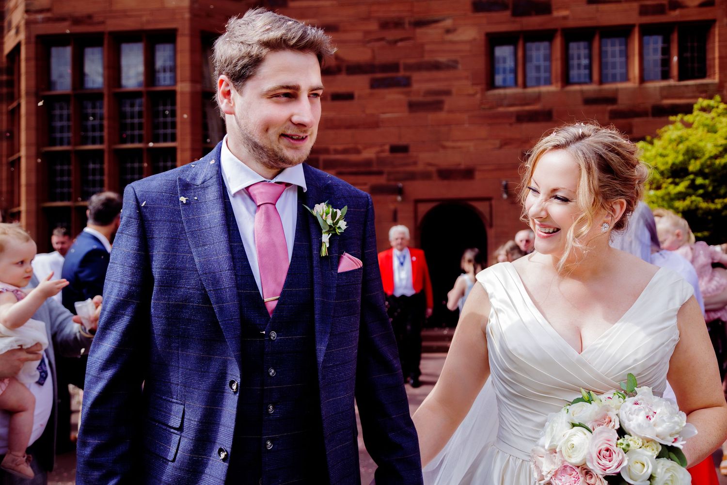A joyful wedding couple exiting their ceremony at a historic brick building.