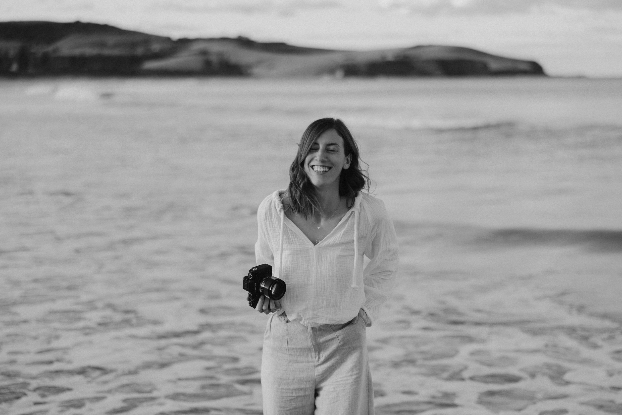 A joyous moment captured at a scenic beach with white clothing and a dramatic coastline in black and white.