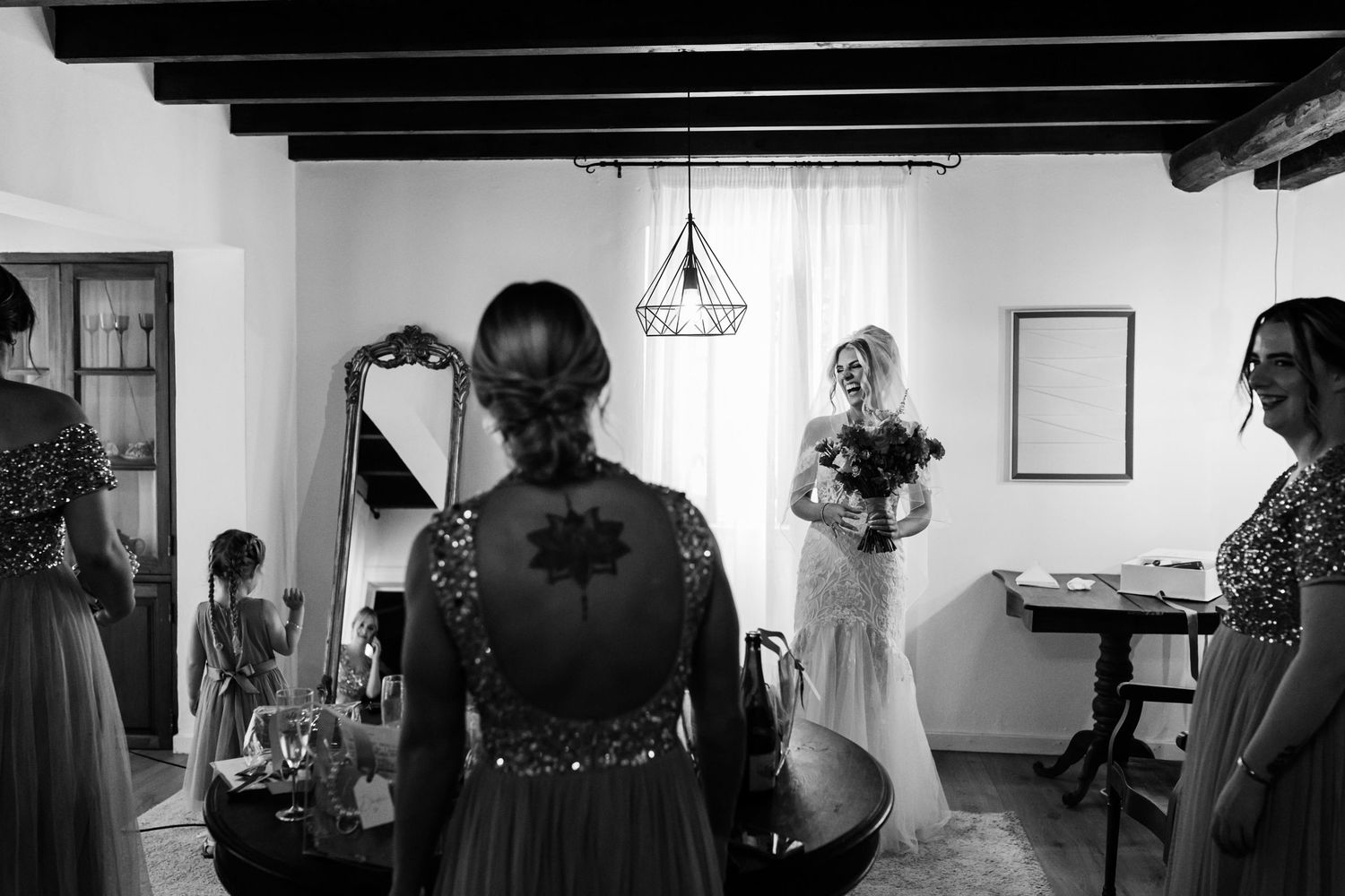 A black and white candid photograph of a bridal preparation scene in a rustic room with exposed wooden beams at Quinta da Bichinha