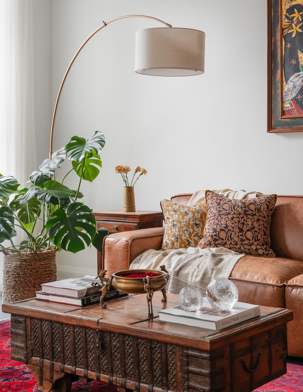 Living room with tan leather sofa, arched floor lamp, and monstera plant on vintage trunk coffee table.
