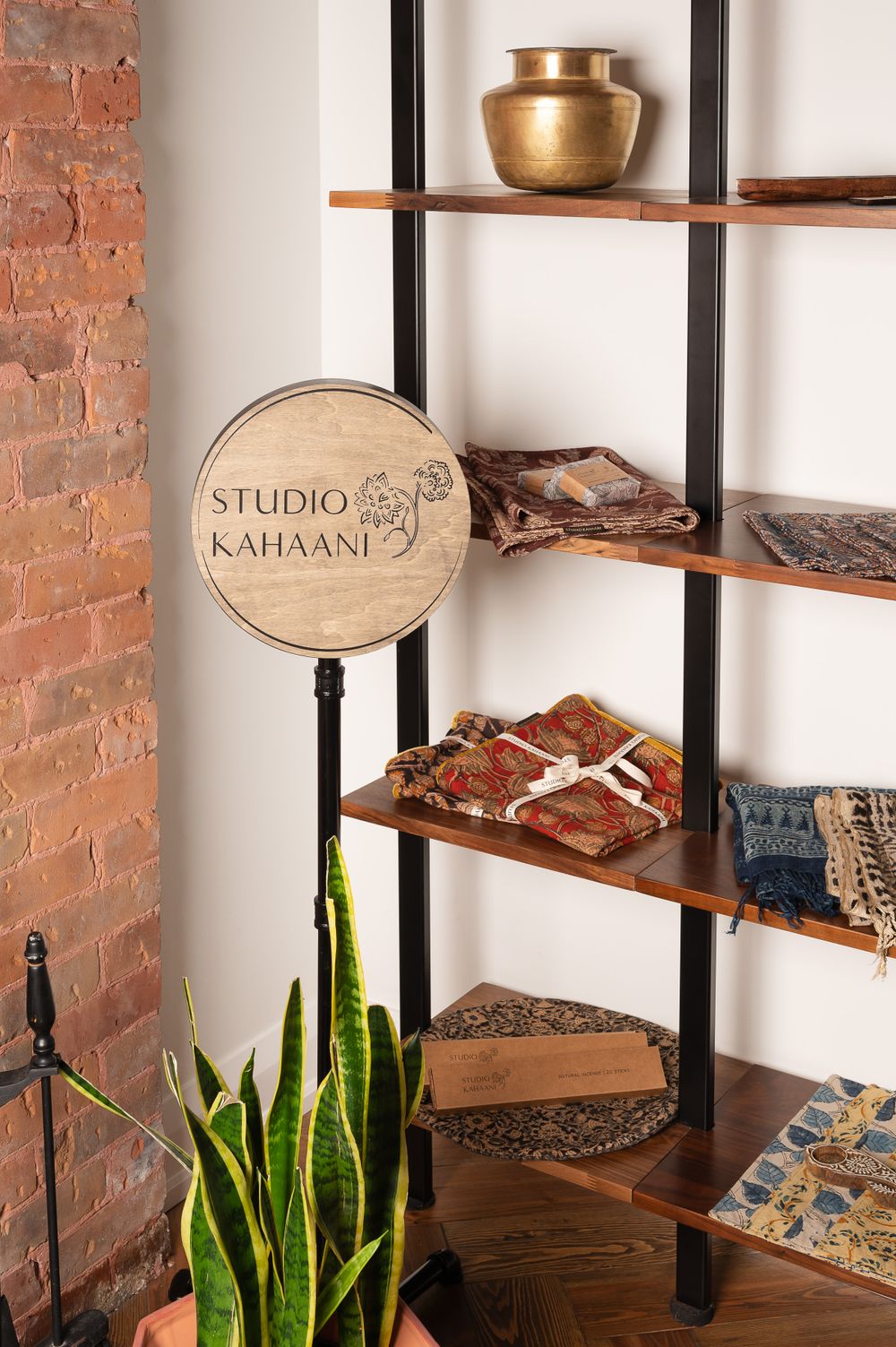 Modern industrial shelving unit with wooden planks displaying decor items and a Studio Kathaant sign.