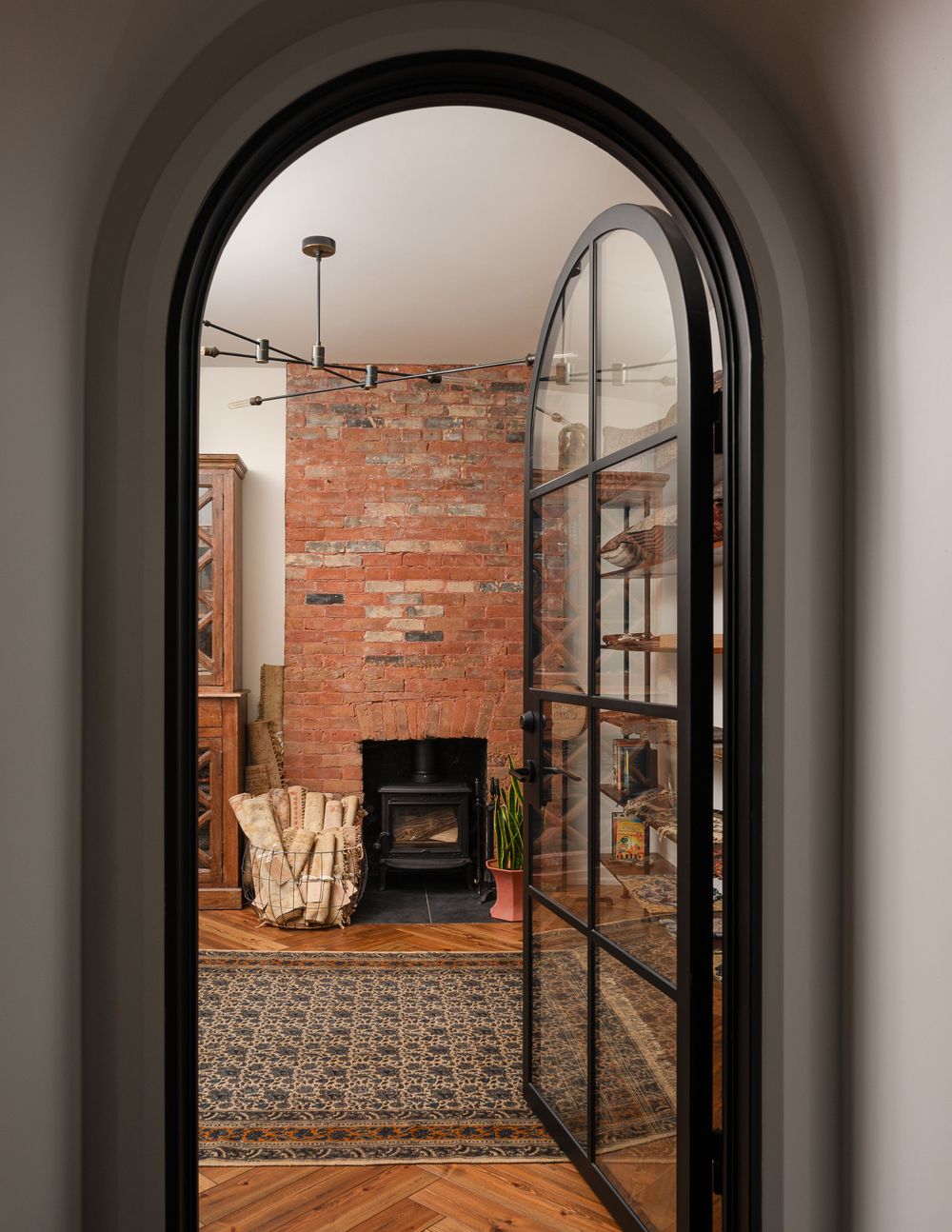 An arched doorway reveals a rustic room with exposed brick walls and a modern fireplace.