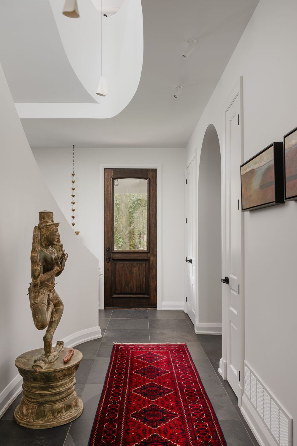A minimalist hallway with arched details, red runner rug, and decorative statue against white walls.