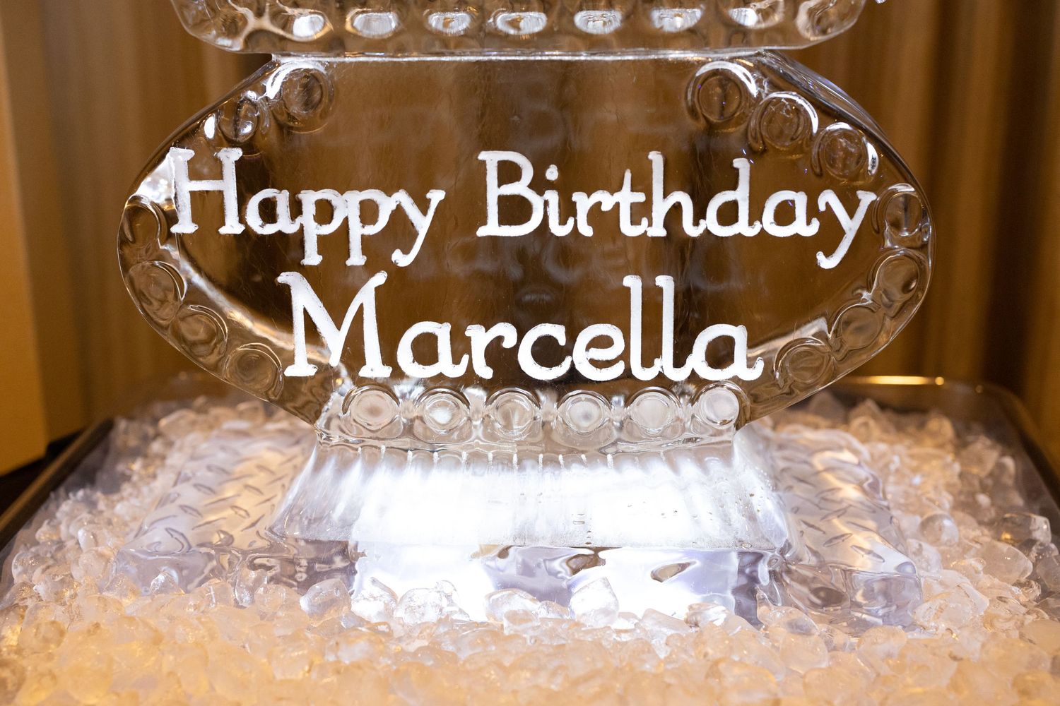 Ice sculpture with 'Happy Birthday Marcella' text elegantly displayed on a crystal stand.
