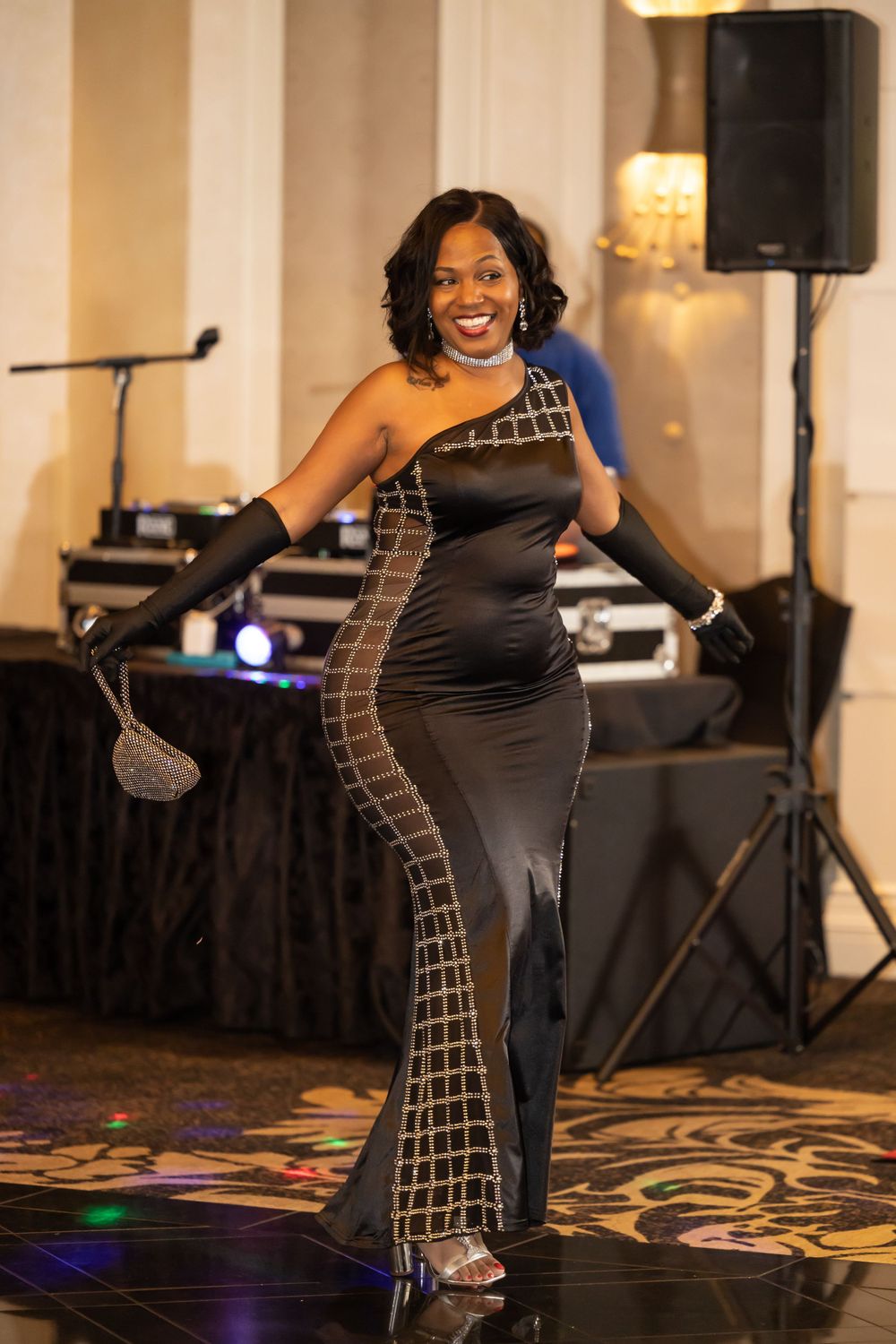 Partygoer strikes a pose in glamorous black gown with silver geometric accents on dance floor.