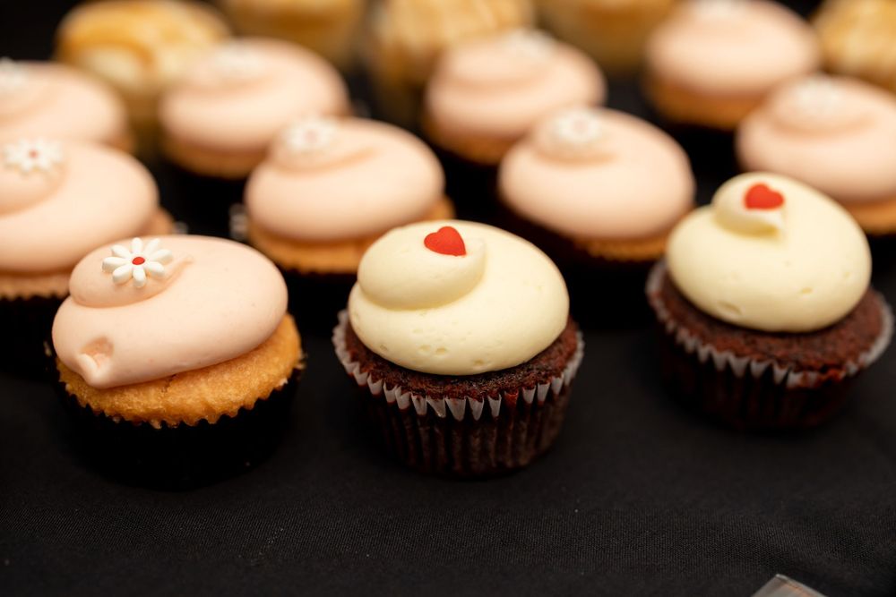 Rows of delicate cupcakes with pink and white frosting topped with small decorative details.