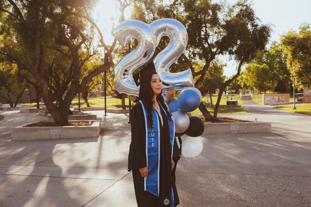 Graduate celebrating with large silver 22 balloons and festive decorations outdoors.