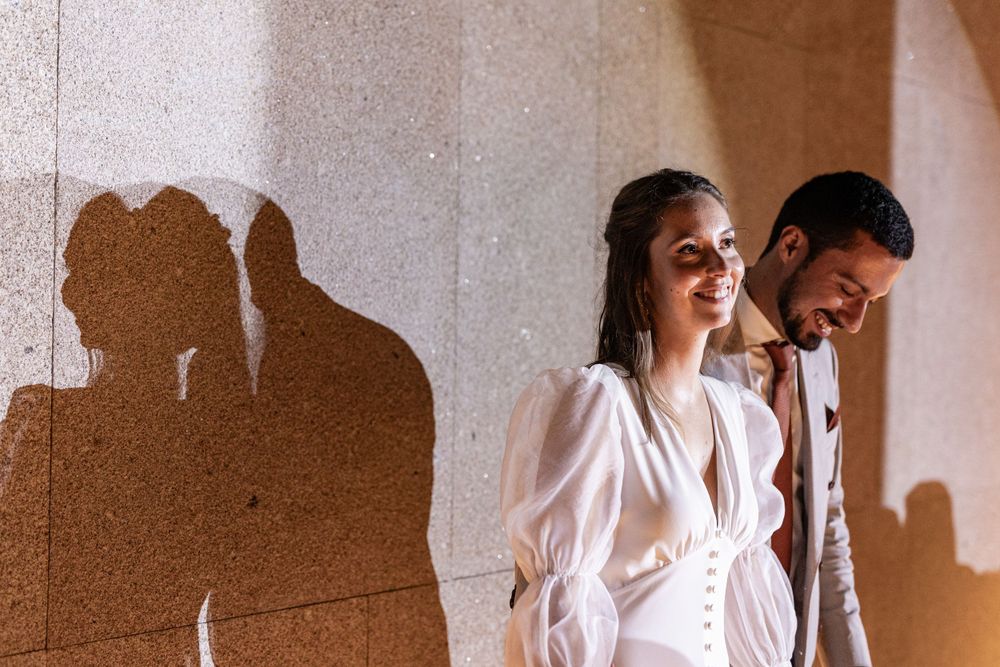 Two people in white clothing standing against a wall with their shadows casting dramatic silhouettes in sunlight at Forte da Crismina, Casca