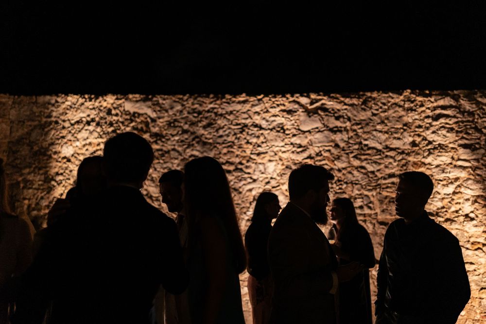 Silhouettes of people standing against illuminated textured stone wall at night.