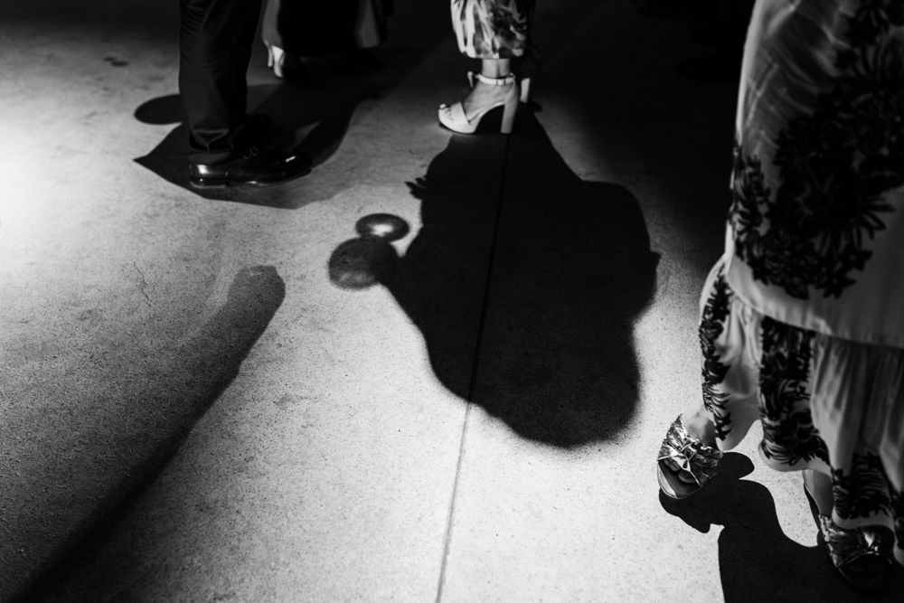 A dramatic black and white photograph showing shadows and feet on a light-colored floor.