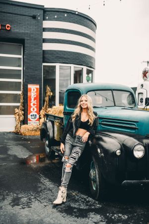 Vintage car and fashion shoot with industrial building and string lights in background.