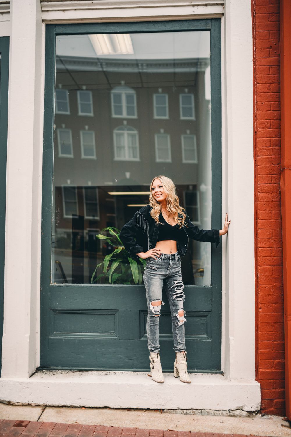 Person poses playfully against white storefront with brick accents and large windows.