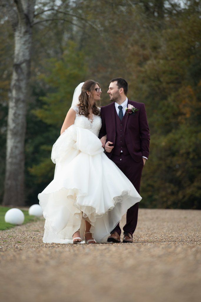 Bride in flowing white dress poses with groom in burgundy suit during autumn wedding.
