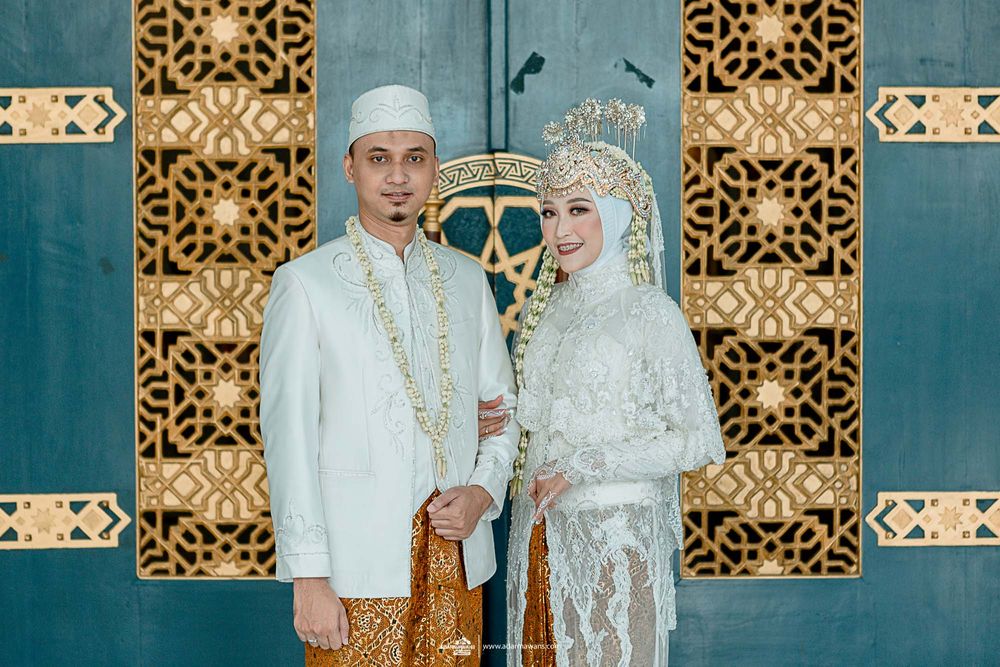 Indonesian wedding couple in traditional white and gold attire pose against geometric pattern backdrop.