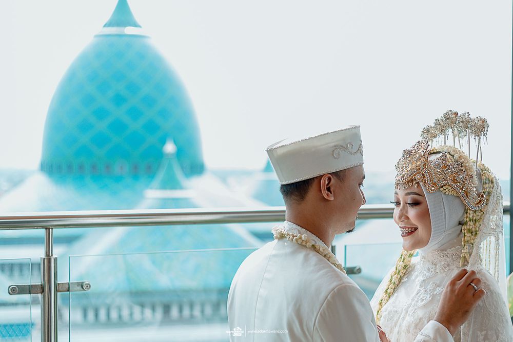 Wedding couple in Islamic attire posing on balcony with blue domed mosque in background.