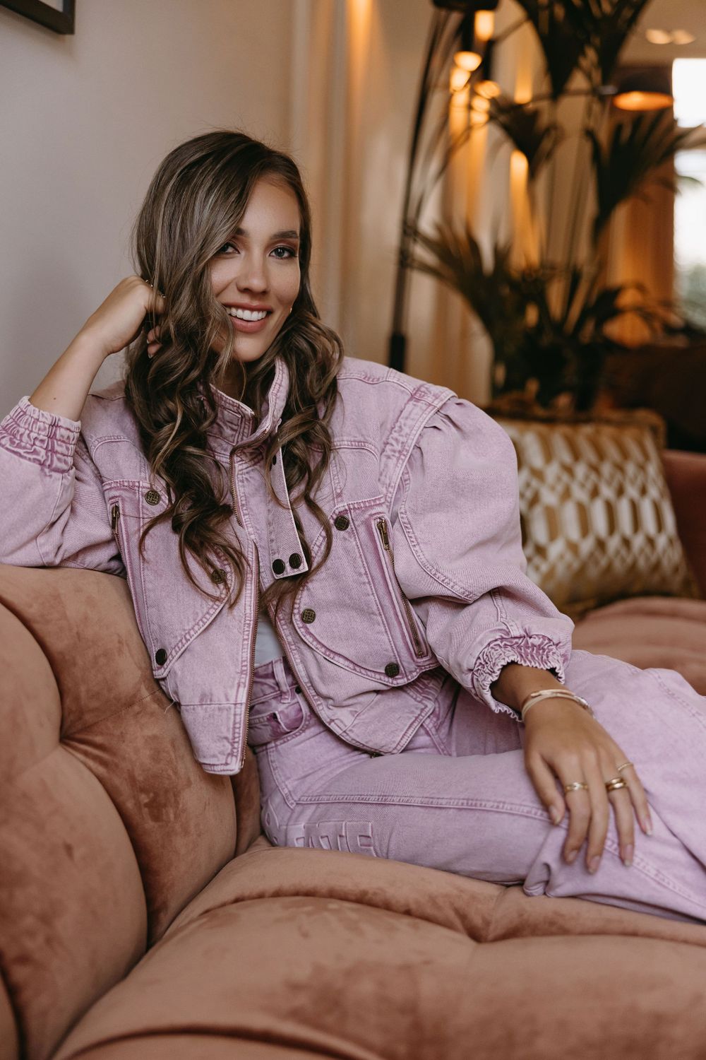 Casual lifestyle portrait in pink denim outfit sitting on brown leather couch.