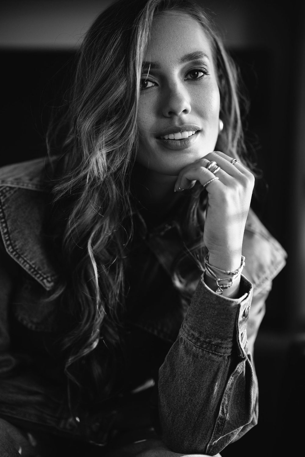 Dramatic black and white portrait with wavy hair and jewelry in denim jacket.
