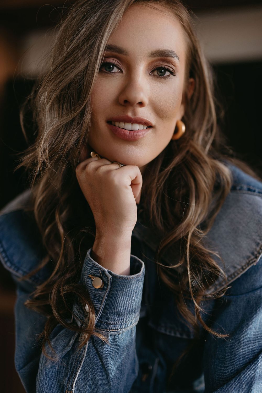 Warm portrait with wavy brown hair and natural makeup in denim jacket.