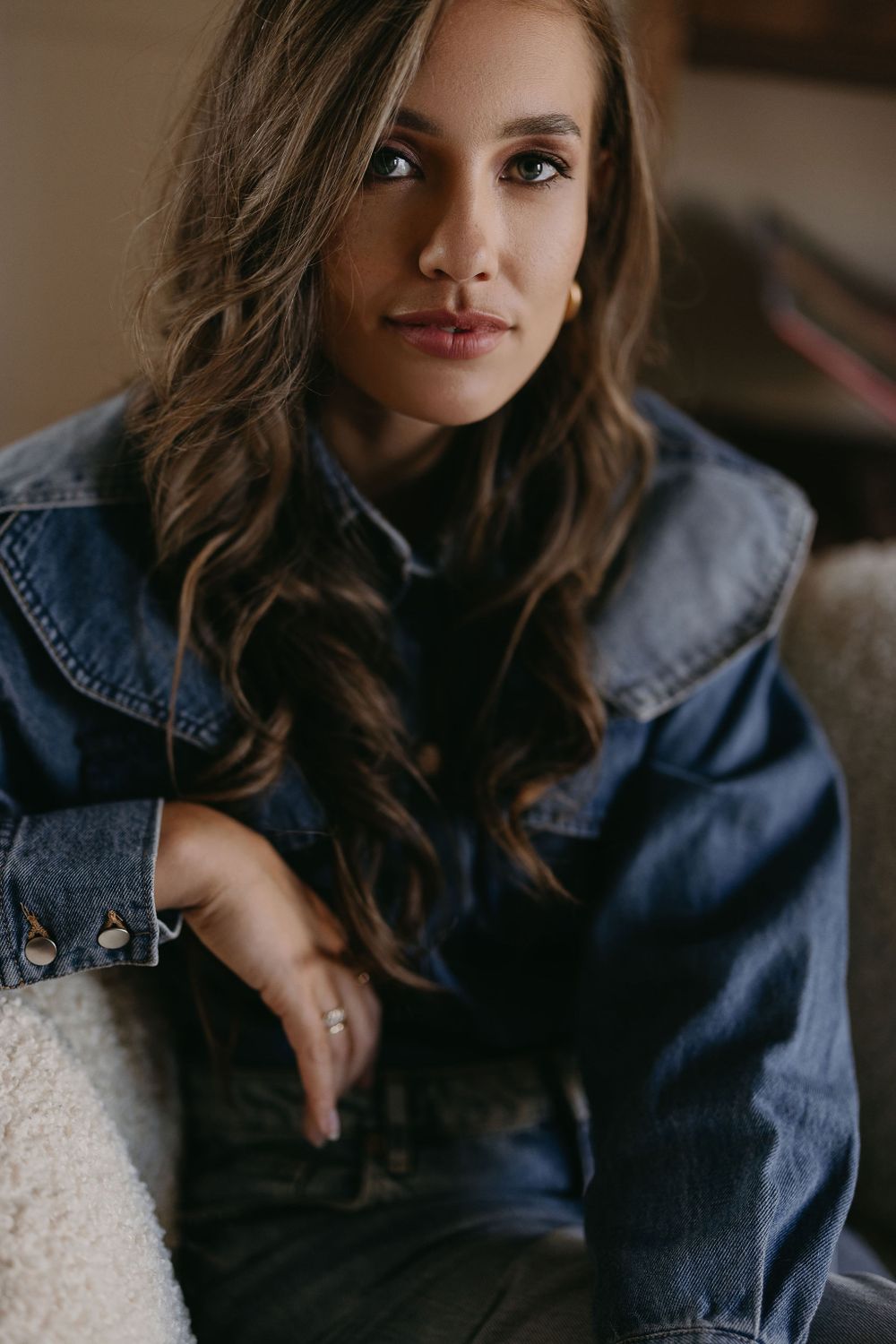 Intimate portrait in denim jacket showing wavy hair and natural makeup.