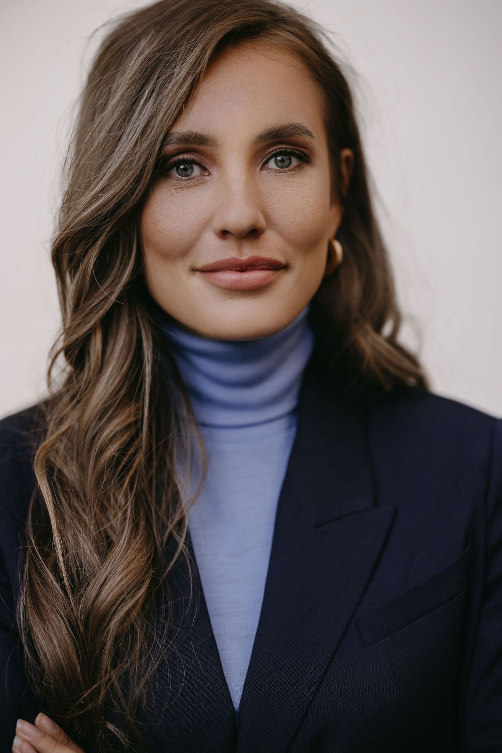 Professional headshot with wavy hair wearing navy blazer and blue turtleneck.