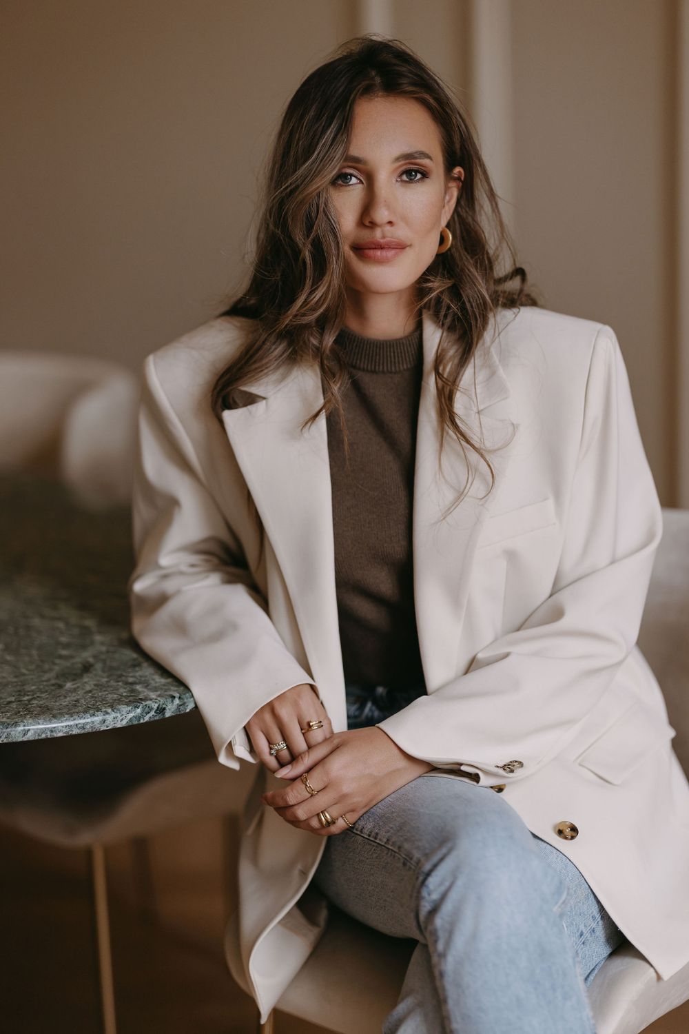 Stylish neutral toned outfit with white blazer and brown sweater in indoor setting.