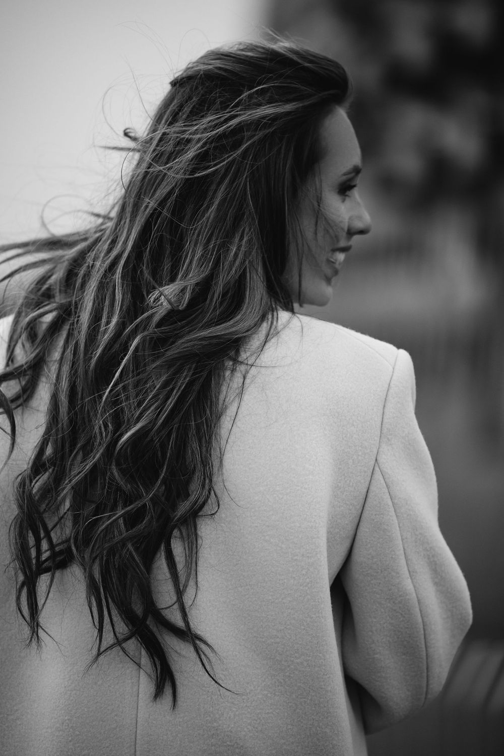 Black and white profile shot highlighting long wavy hair and elegant white blazer.