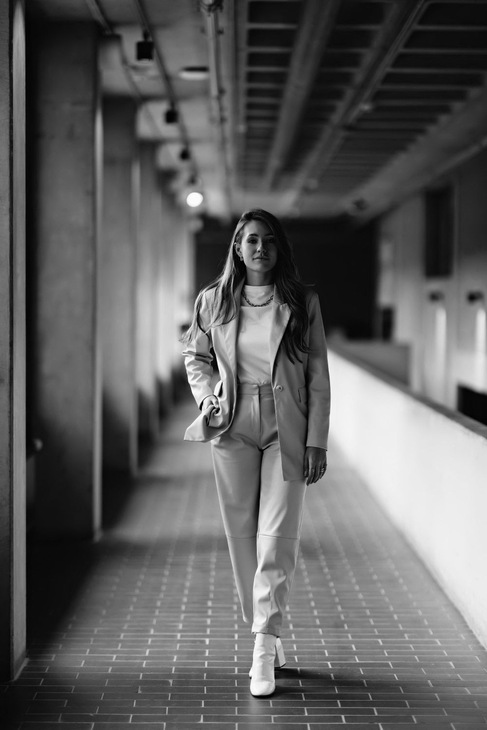 Model walking down corridor in all-white pantsuit and blazer ensemble.