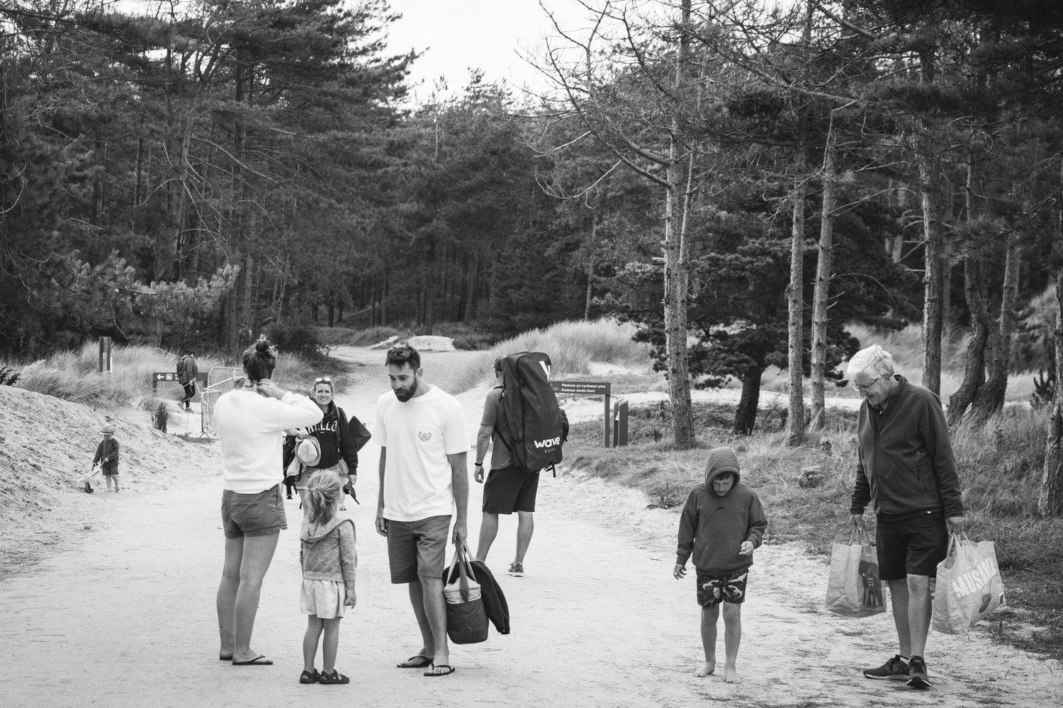 A black and white photo showing people walking along a wooded path on a sunny day.