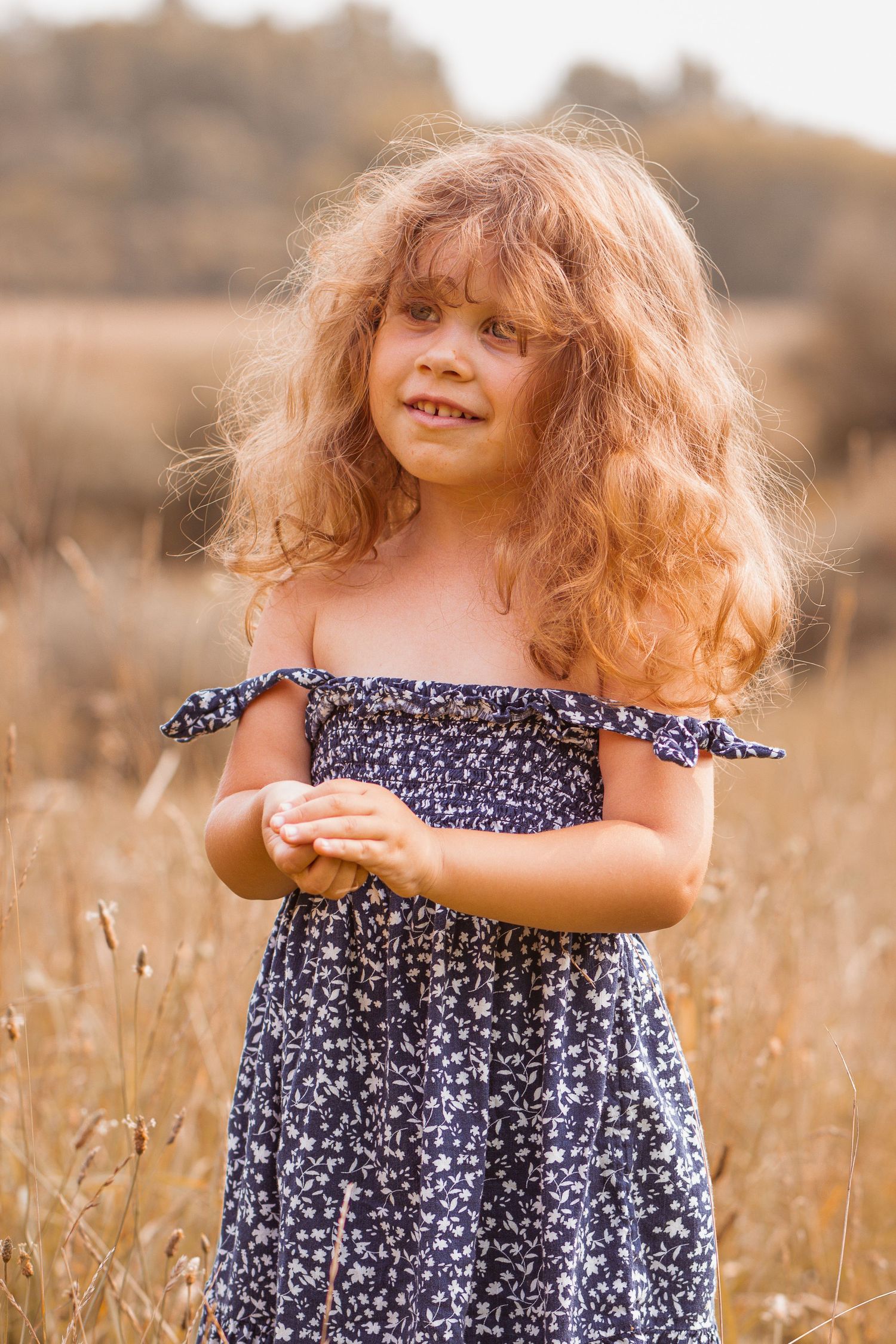 Child in navy floral dress playing in golden summer field.