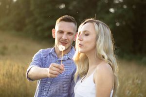 Adorable couple blowing dandelions at maternity photoshoot