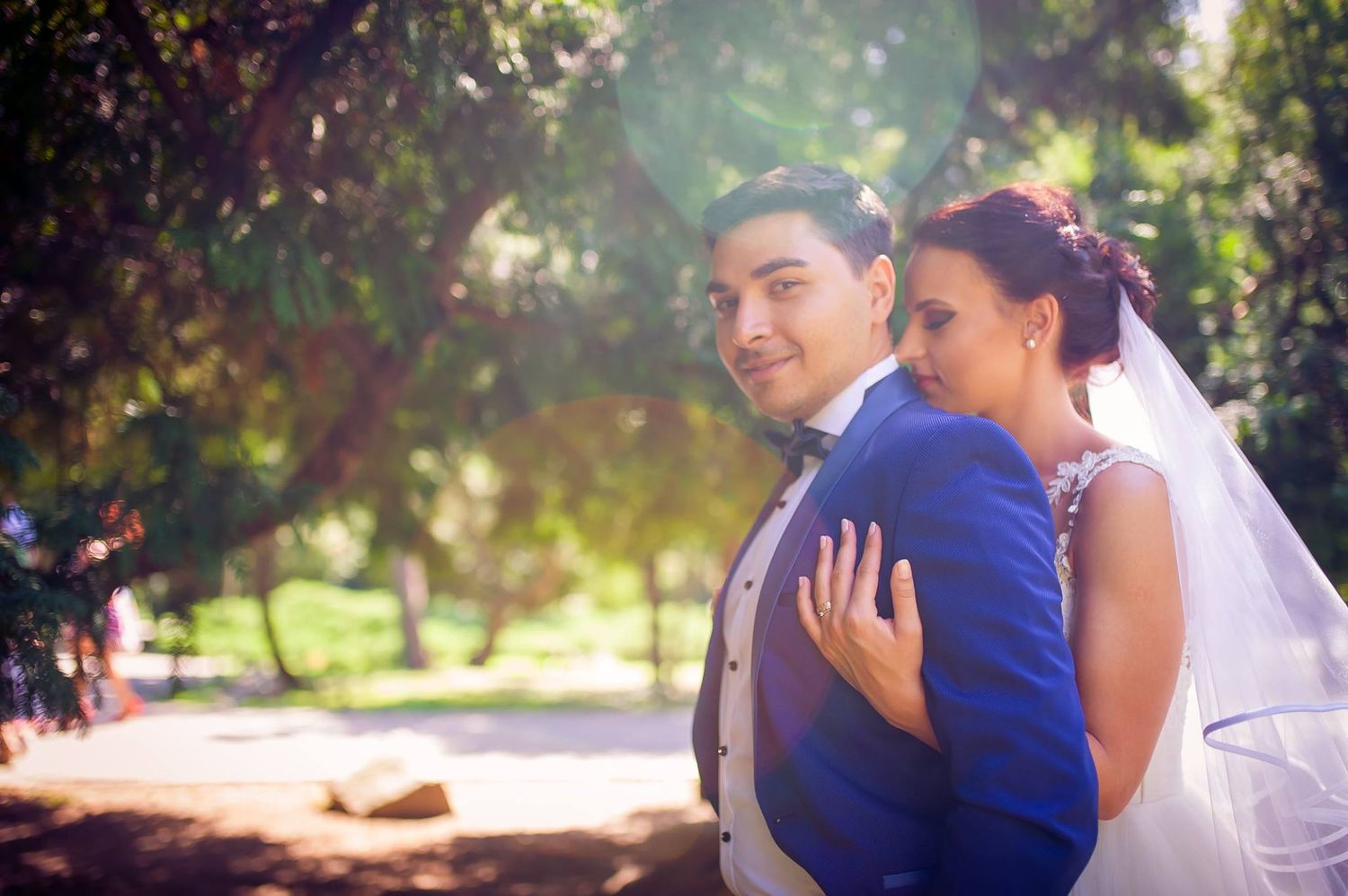 Joyful wedding couple embracing in sunlit garden setting.
