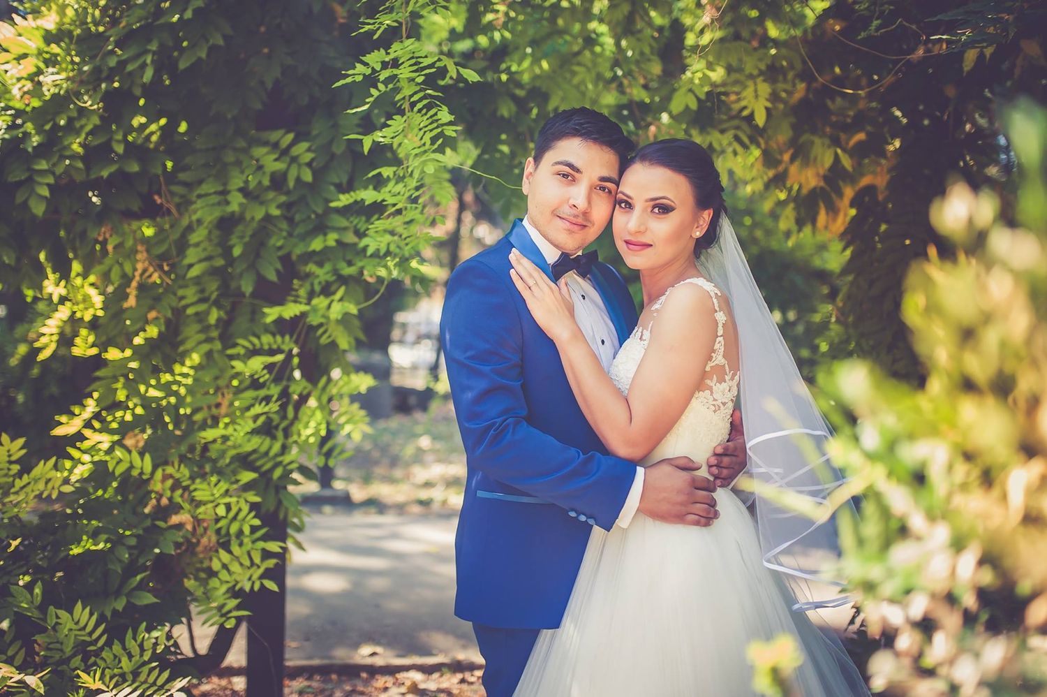 Wedding couple in blue suit and white dress embracing in garden setting.