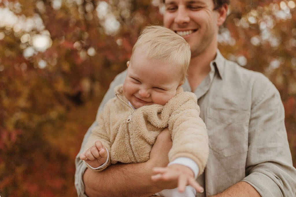 8 month old baby boy smiling cheekily in the arms of his dad