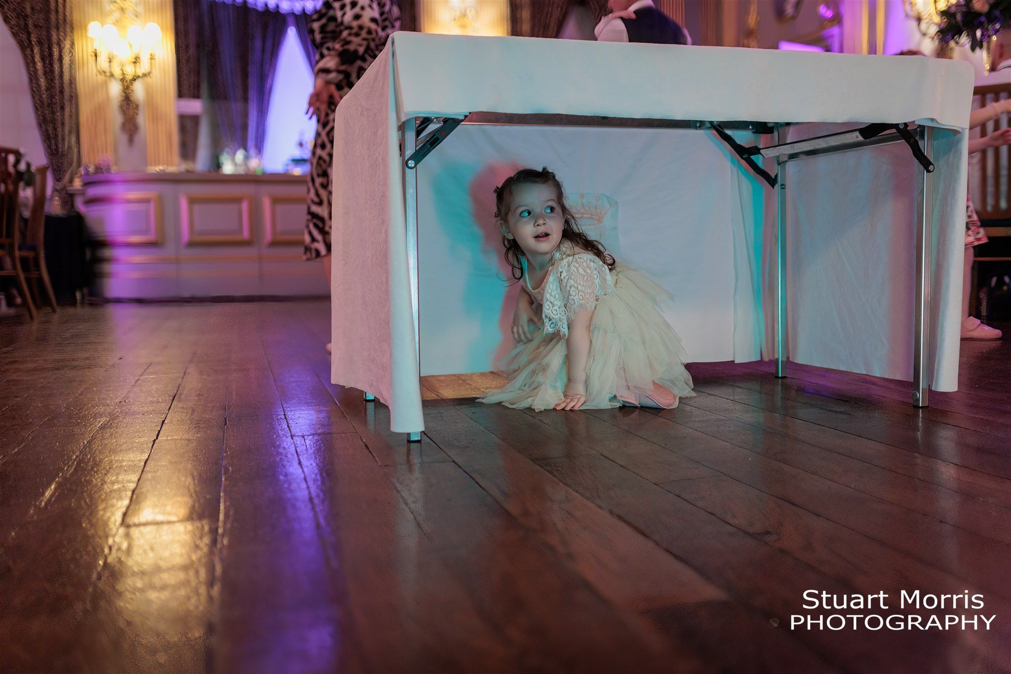 Young girl hides under the wedding cake table. Knowsley hall wedding photography. Liverpool Wedding photographer.