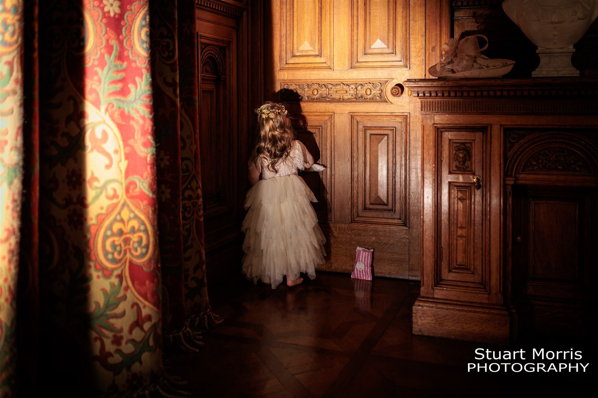 Young flower girl goes and stands in a wood panelled corner of Knowsley hall Liverpool wedding venue.