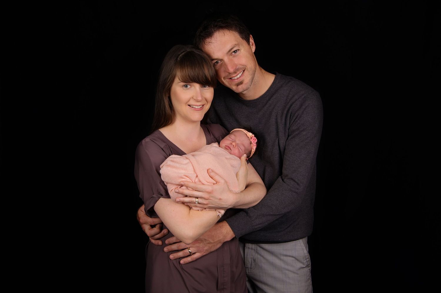 mother and father embracing newborn baby girl wrapped in peach colours