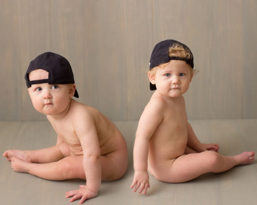 Two studio shots of a baby wearing a backwards baseball cap while sitting on the floor.
