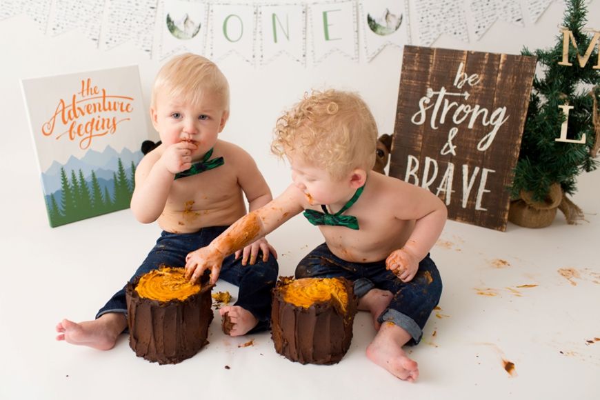 Toddlers in jeans enjoying messy cake smash session with orange frosting.
