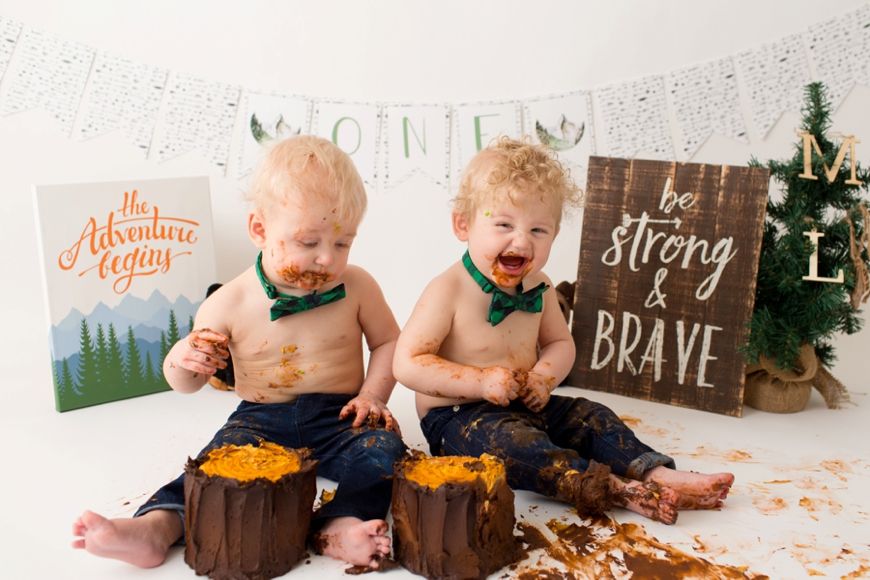 Excited toddlers during cake smash photoshoot with woodland themed backdrop.