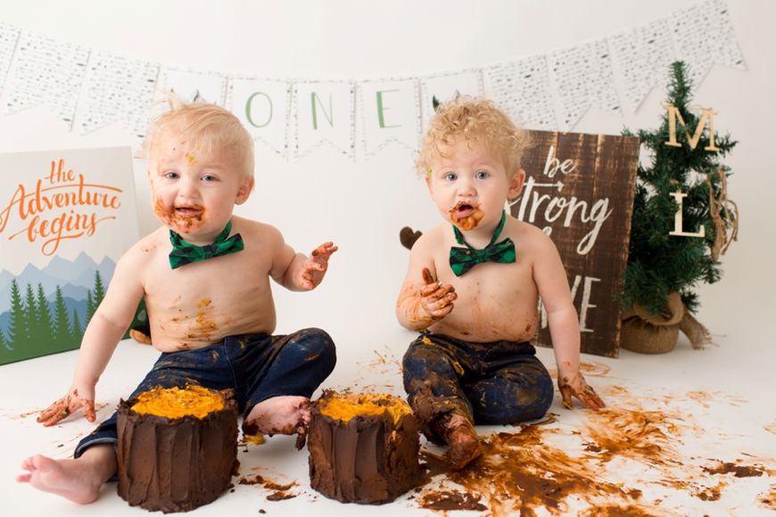 Two excited children during cake smash session with orange frosted cakes.