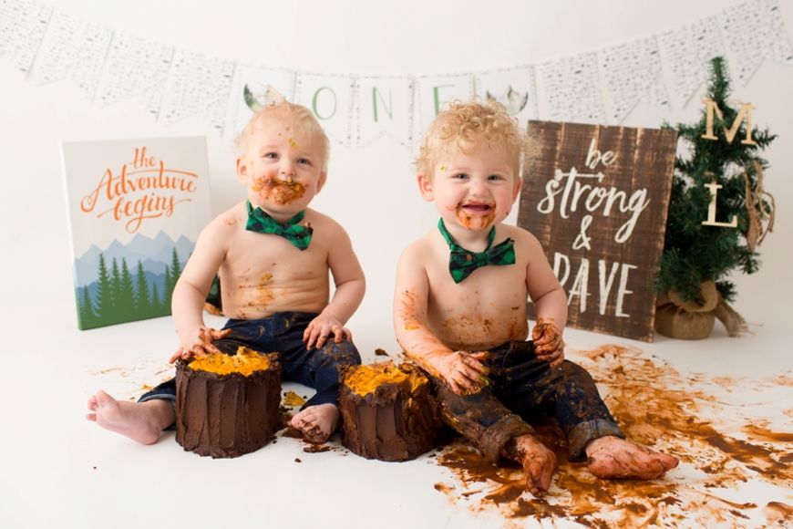 Festive cake smash photo setup with twin babies, Christmas tree and decorative wooden signs.